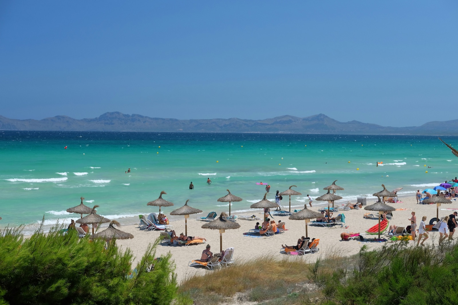 Pláž Playa de Muro s tyrkysovým morom a slamenými slnečníkmi