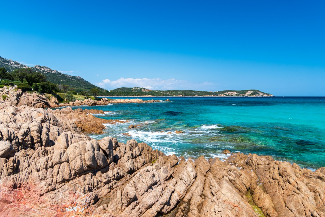 Skalnaté pobrežie a tyrkysové more pri pláži Grande Pevero na Costa Smeralda