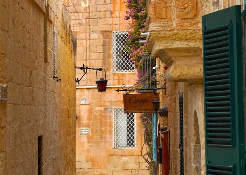 Úzka ulička s kamennými domami a kvetmi v meste Mdina na Malte