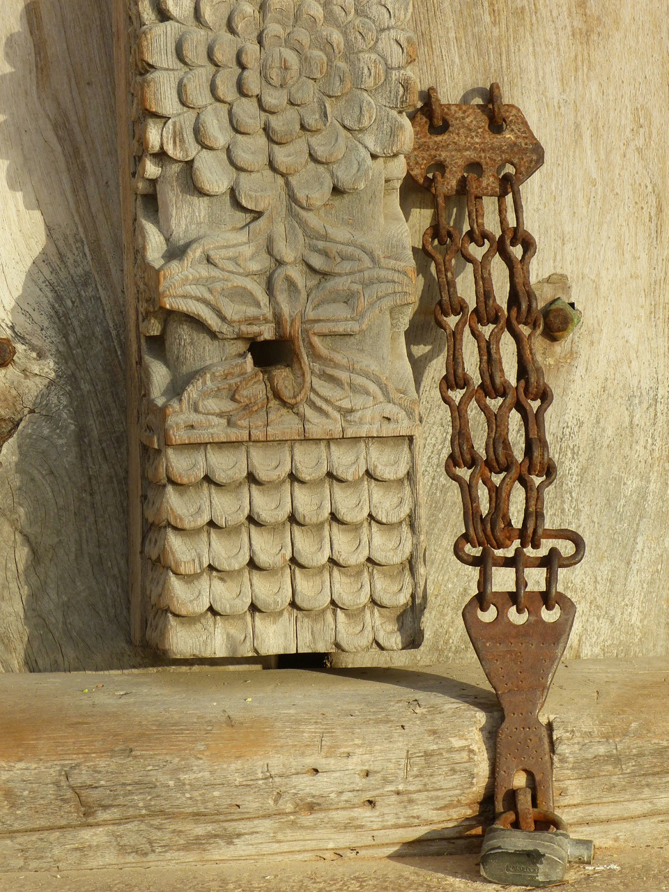 Rezbovaný drevený detail dverí s reťazou v Stone Towne